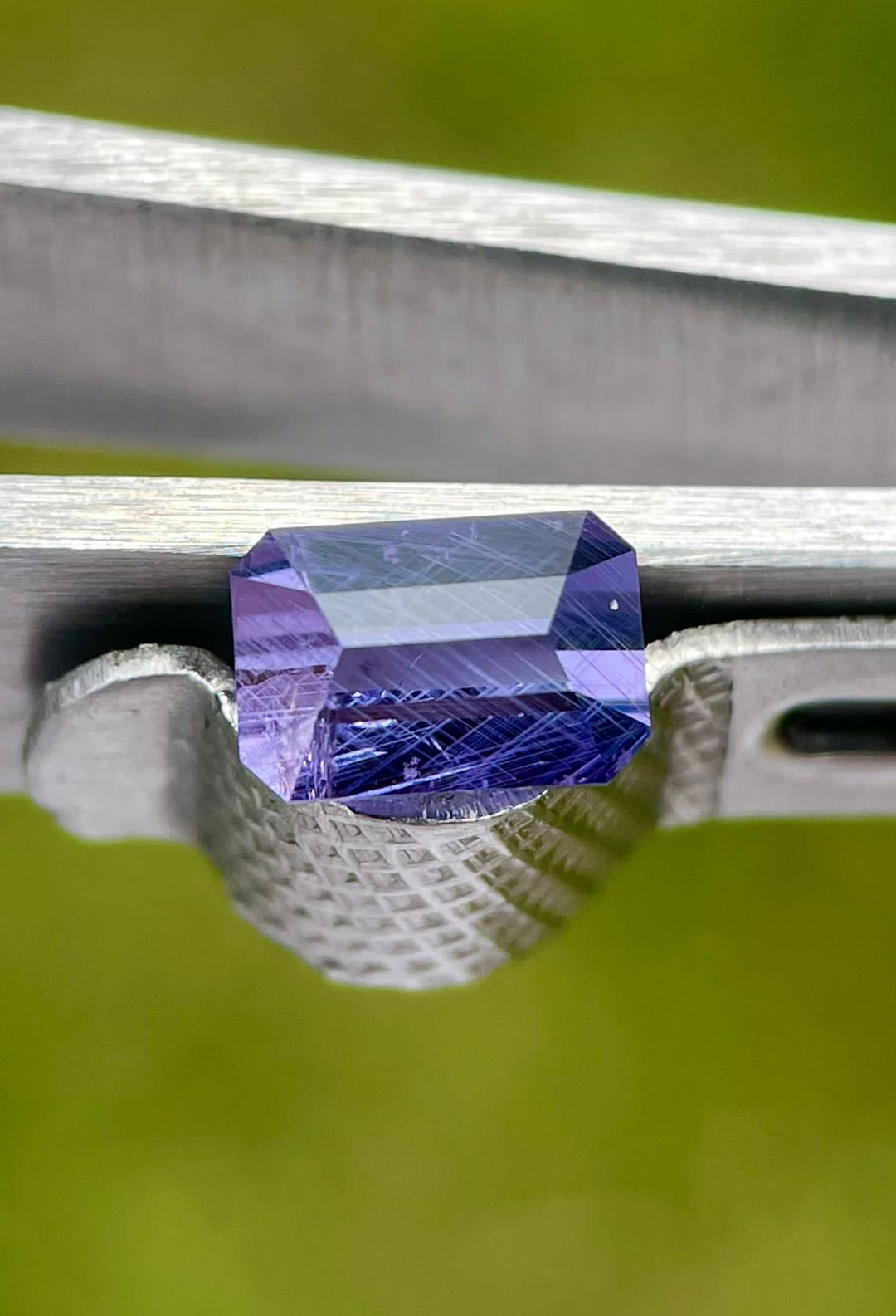 Detailed image of a Royal Amethyst No Heat Sapphire secured by calipers, highlighting the precise dimensions and unique purple hue of the custom modified emerald cut gemstone from Tanzania
