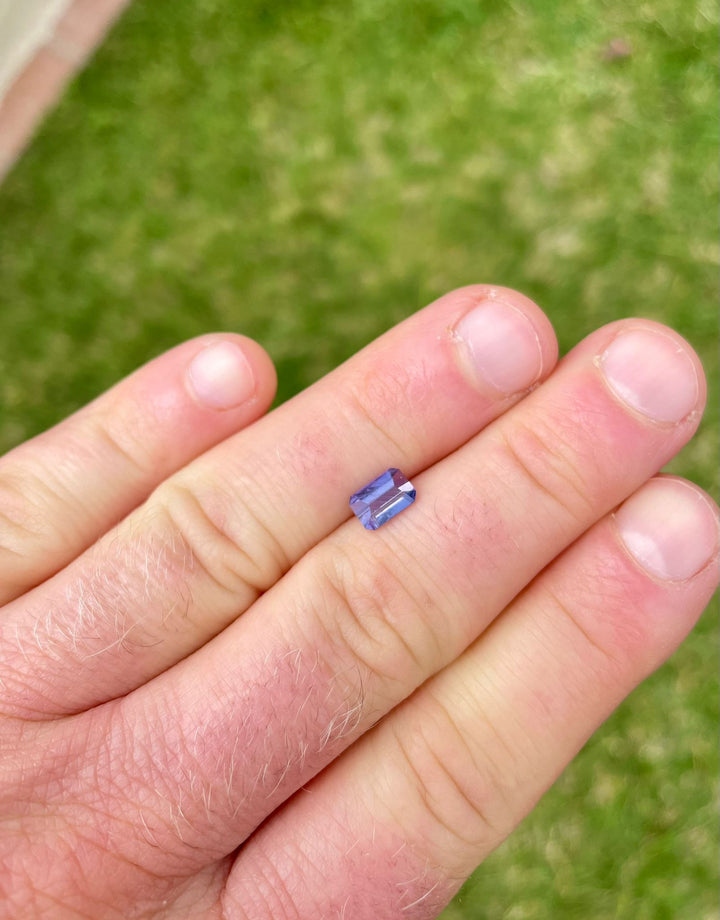 Close-up view of a 1.37-carat Royal Amethyst No Heat Sapphire in the hand, showing its custom modified emerald cut and vibrant purple color, sourced from the Umba River, Tanzania.