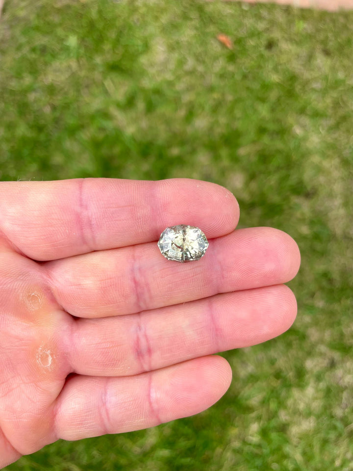 Hand-held view of a large 7.14-carat sapphire from Tanzania, demonstrating its unique color-changing properties from teal blue green to greenish peach, and its precise dimensions.