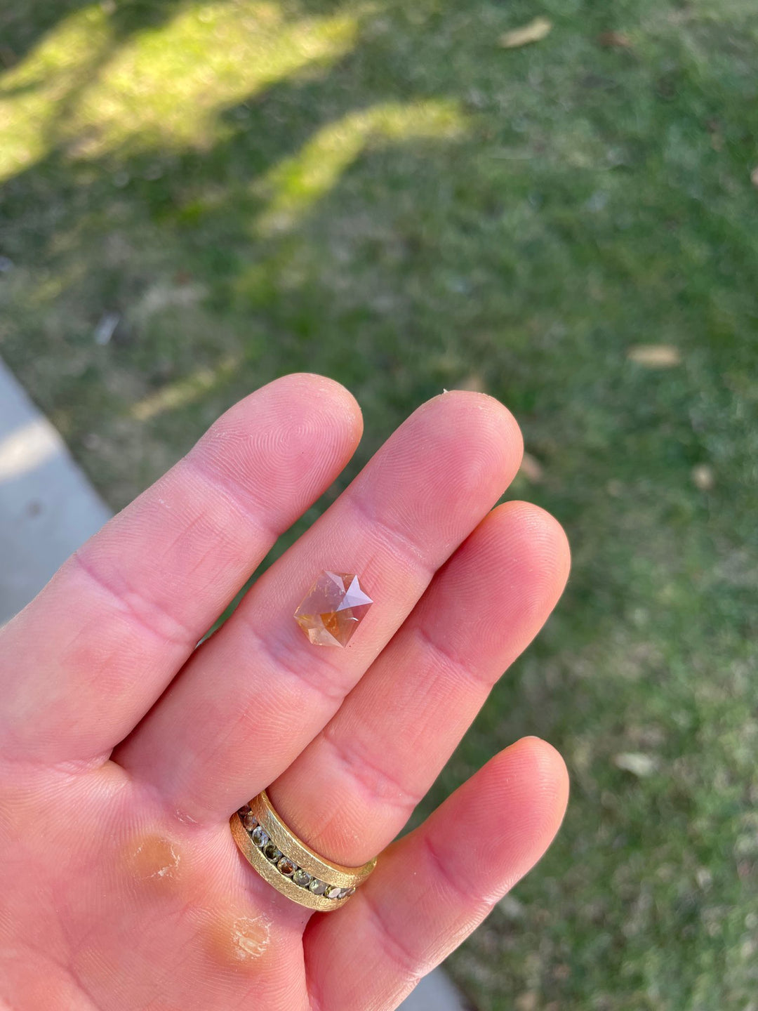 Hand-held view of a multicolored sapphire, emphasizing its unique hexagon rose cut and vibrant colors ranging from amber to mauve. The gemstone, weighing 3.12 carats and sourced from Tanzania, showcases its natural, untreated beauty.