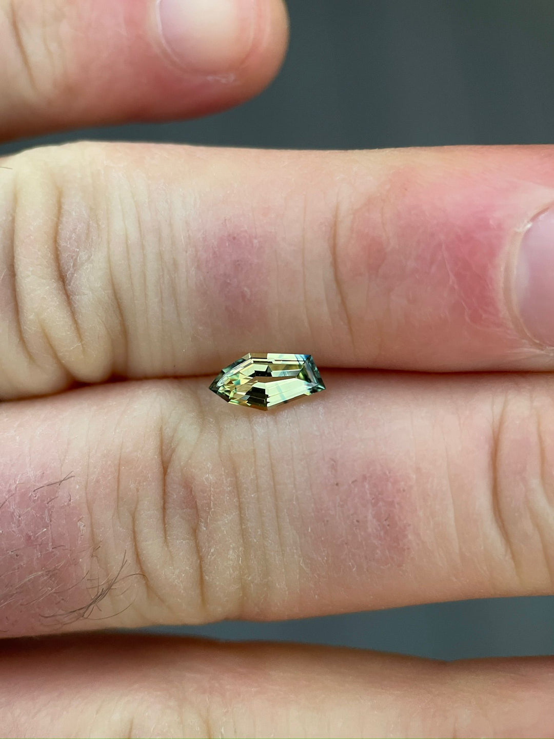 Close-up of a 0.80-carat yellow-blue sapphire resting on a human hand, highlighting the gem's freeform geometric shape and natural, untreated appearance.