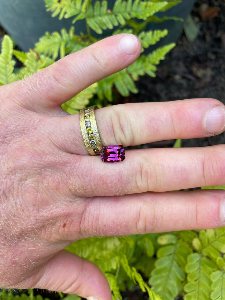 Vibrant 4.29-carat garnet displayed on a finger ring against a lush fern background, emphasizing its deep purple, pink, and red hues with a geometric modified cushion cut from Mombo, Tanzania.