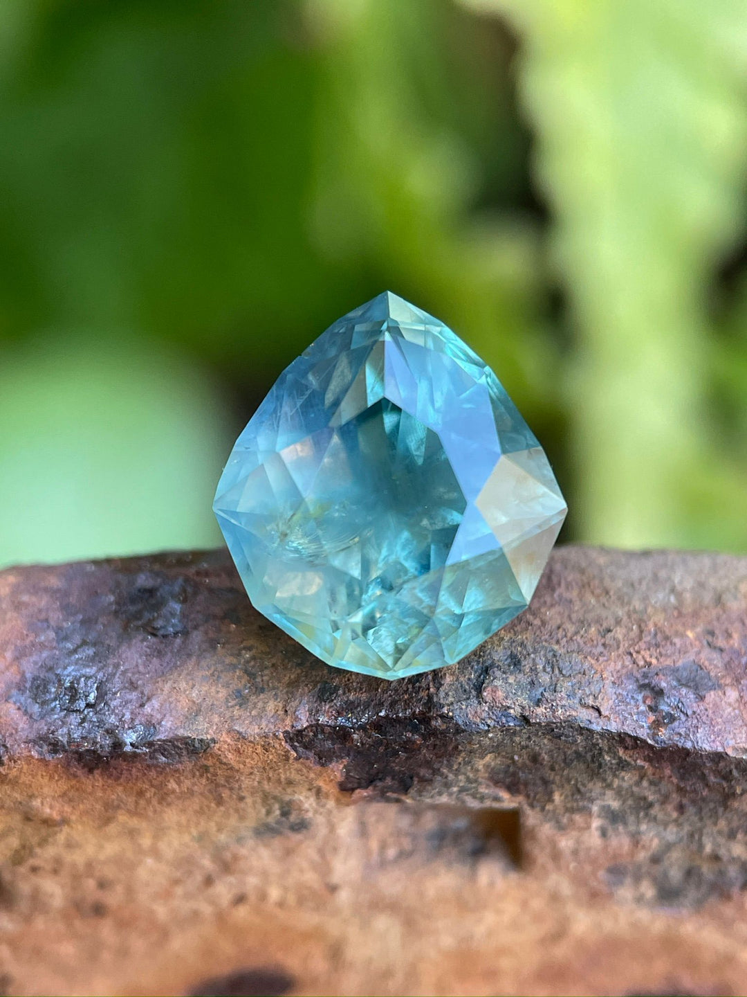 7.08-carat silky blue, green, and teal sapphire in a custom geometric pear shape. This high-clarity gemstone from Montana showcases its unique shape and natural colors, emphasizing its untreated state.