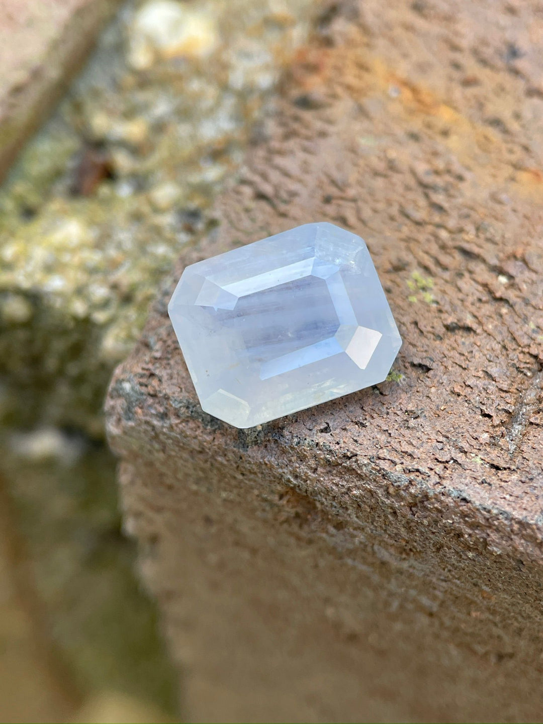 Exquisite 5.10-carat Sri Lankan sapphire with an octagonal emerald cut, delicately placed on a rustic surface, highlighting its unique opalescent color blend and precise cut.