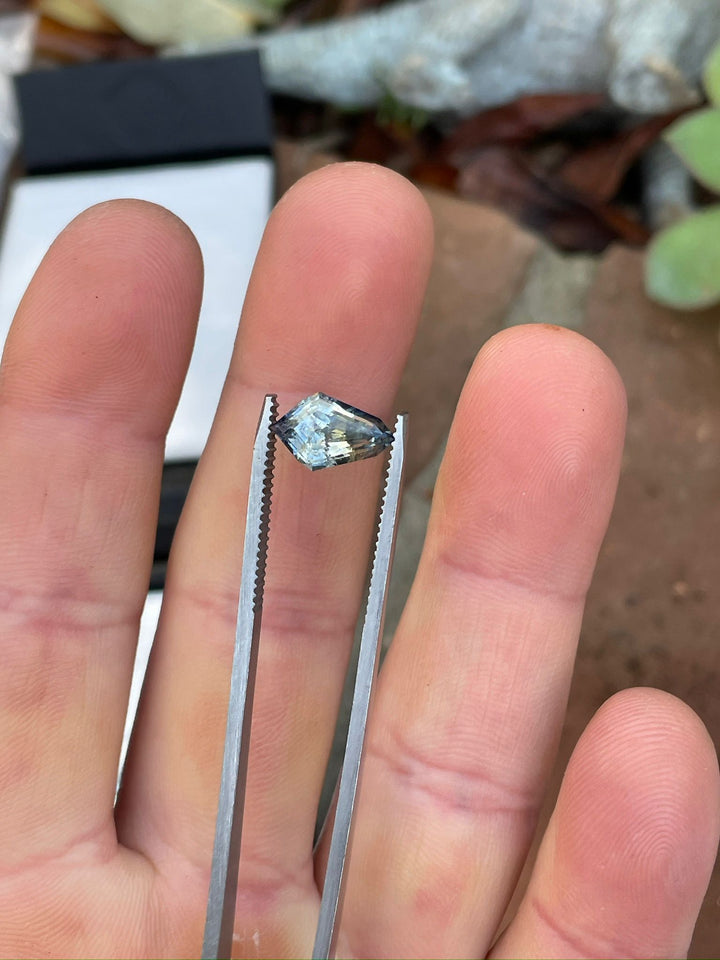 Close-up of a 2.32-carat Sri Lankan sapphire in geometric step cut kite shape, displayed on a human hand, highlighting its vibrant yellow and Ceylon denim hues.