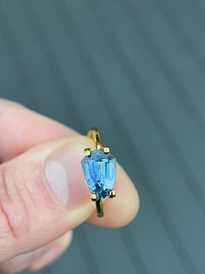 Elegant 1.53-carat custom shield step cut sapphire, held delicately in fingers, exhibiting parti colors of denim, cornflower, and teal, sourced from the Umba River, Tanzania.