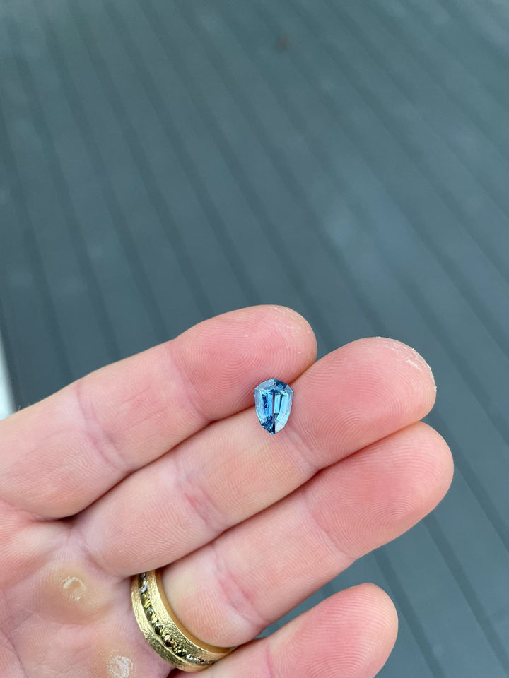 Close-up of a 1.53-carat Tanzanian sapphire with a unique shield step cut, resting on a person's hand, displaying vibrant parti colors against a blurred background.