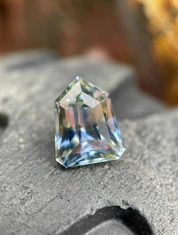 Exquisite 2.74-carat custom step cut shield Sri Lankan sapphire, displayed on a slate background, featuring a unique blend of yellow, cornflower, and parti colors.