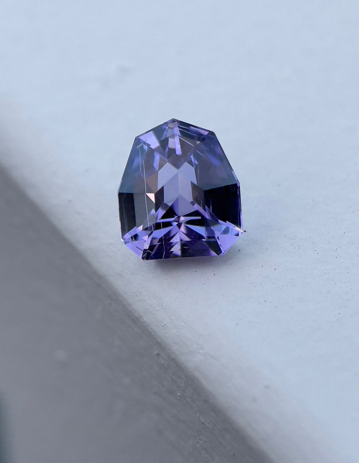 Vivid 3.19-carat Tanzanite gemstone with a custom geometric shield cut, prominently displayed on a gray surface, showcasing its brilliant blue, purple, and lavender hues.