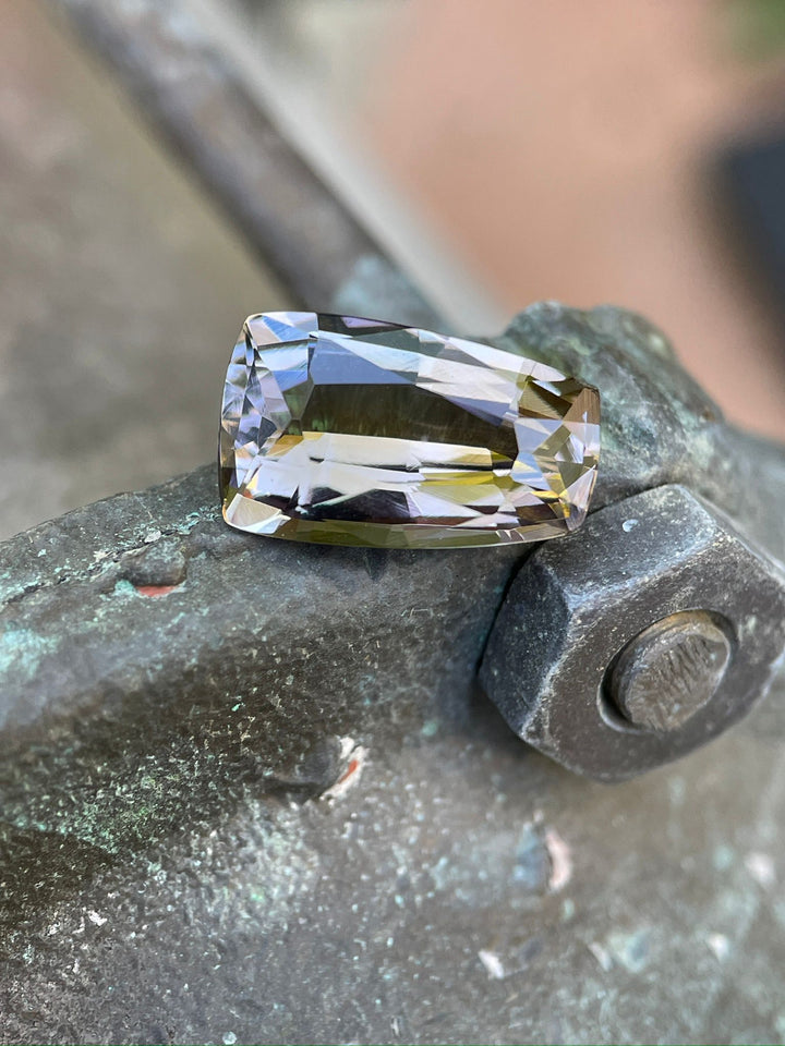 Exquisite 4.98-carat Tanzanite with a custom tapered shield mix cut, resting on a mossy rock, displaying rich purple and champagne colors, sourced from the Merelani Hills, Tanzania.