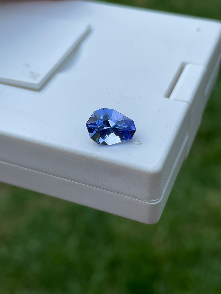 Vibrant ultra violet blue Tanzanite gemstone, weighing 2.26 carats and cut in a unique geometric teardrop shape, displayed on a clean white box, reflecting its exquisite facets and deep color, originating from Merelani Hills, Tanzania.