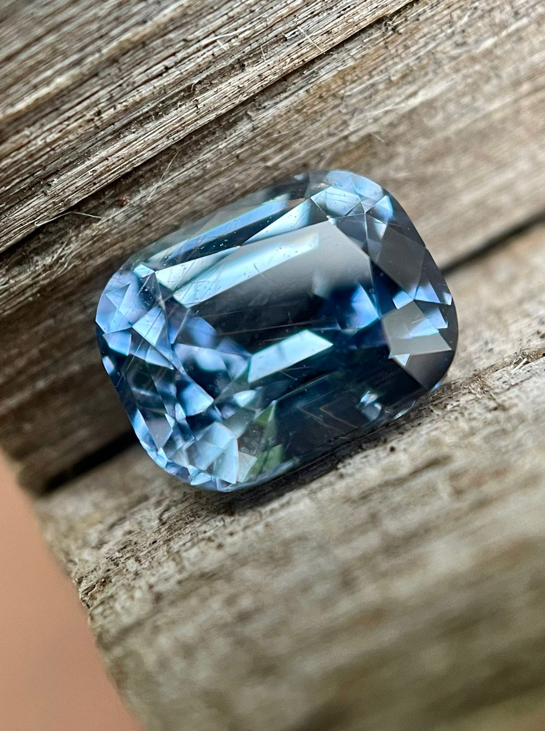 Tanzanian sapphire with a classic precision cushion cut, set against an aged wood backdrop, emphasizing the gem’s color-shifting property from teal indigo to violet.