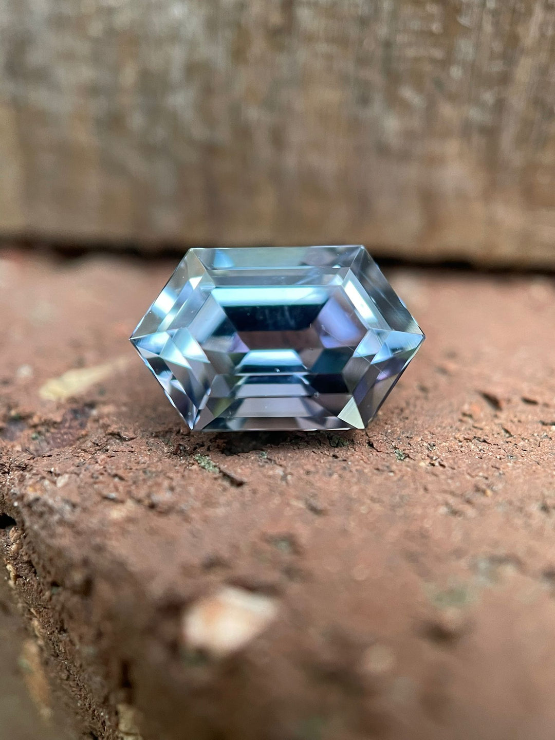 Tanzanite gemstone resting on a textured brick surface, showcasing its unique step cut hexagonal shape and mesmerizing color transition from teal to purple to blue. Weighing 1.79 carats and sourced from Merelani Hills, Tanzania, this gem measures 9.54 x 6.38 x 4.38 mm and is valued at $1700.50.