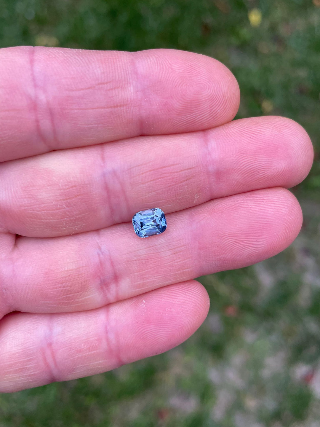 A 1.42-carat color-shifting sapphire from Tanzania, held gently in a person's hand, showcasing the gem's classic precision cushion cut and its teal indigo to violet hues.