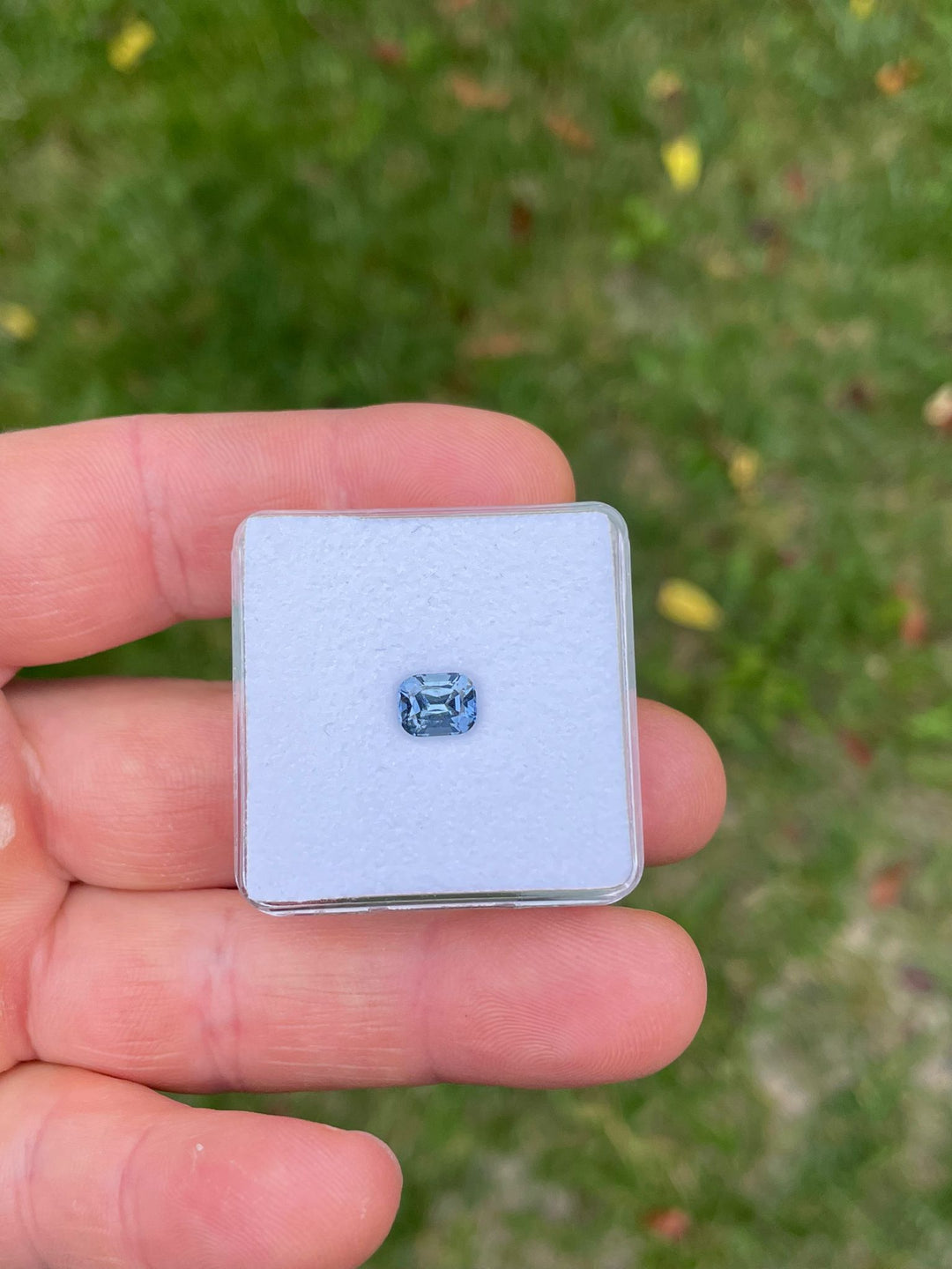 Close-up view of a Tanzanian sapphire on a white display case, illustrating the vivid color transition from teal indigo to violet in natural lighting, weight 1.42 carats.