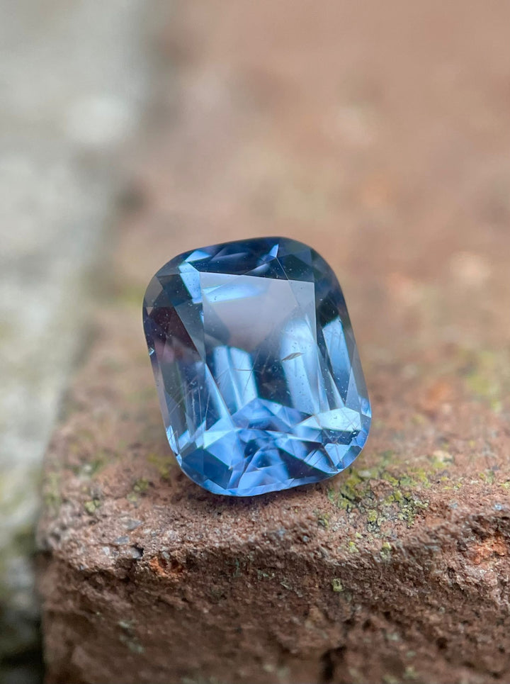Detailed image of a 1.42-carat color-shifting sapphire from the Umba River, Tanzania, placed on a rustic brick surface, highlighting its unique cushion cut and vibrant colors.