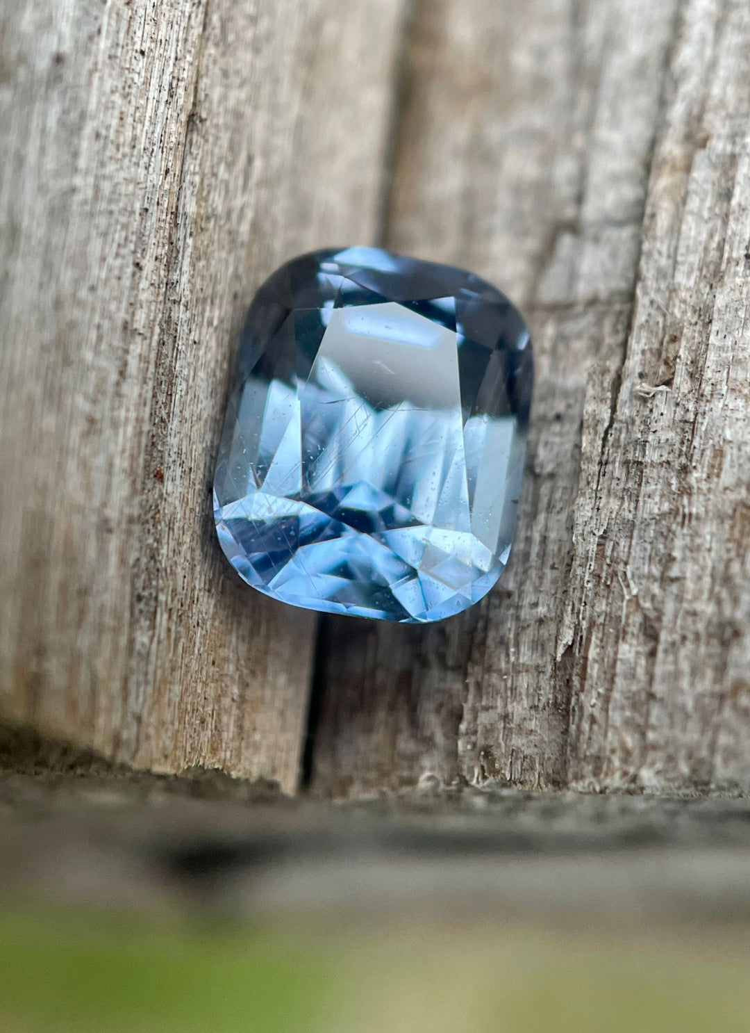 Vibrant Tanzanian sapphire showcased on a natural wood background, featuring a 1.42-carat weight and a color-shifting appearance from teal indigo to violet under daylight.