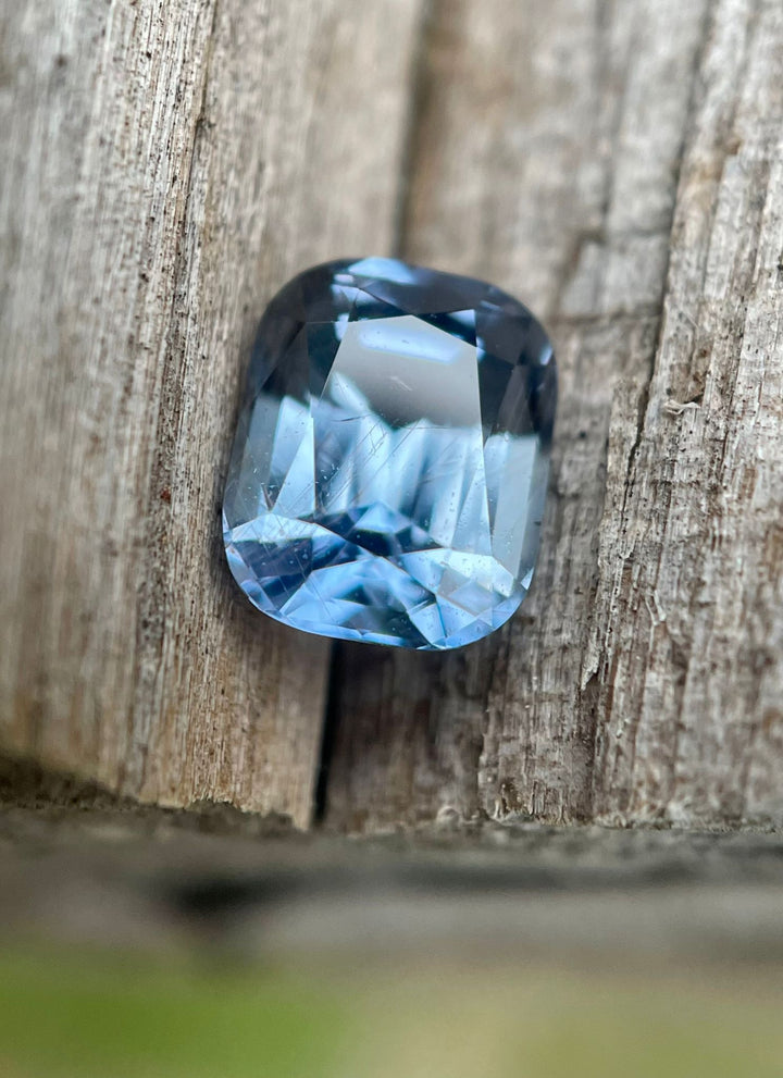 Vibrant Tanzanian sapphire showcased on a natural wood background, featuring a 1.42-carat weight and a color-shifting appearance from teal indigo to violet under daylight.