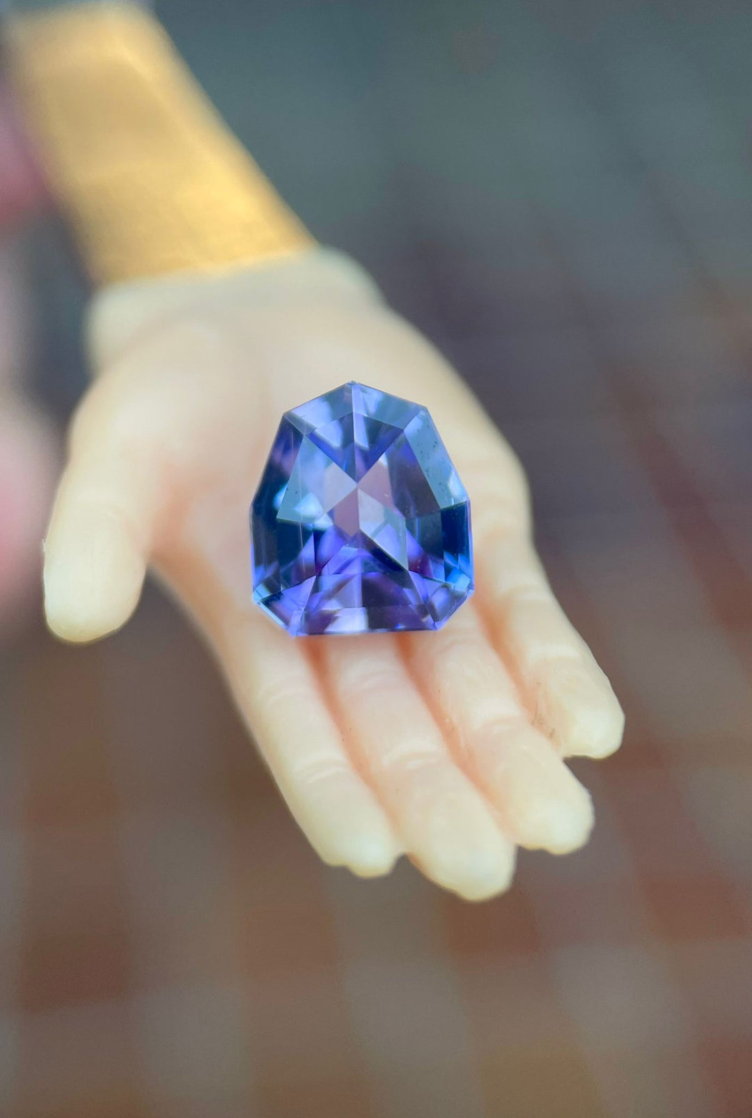 Elegant Tanzanite gemstone held delicately in a person's hand, featuring a unique geometric shield cut and displaying deep blue, purple, and lavender shades.