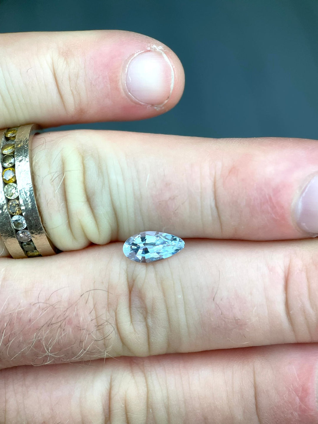 Close-up of a 1.42 carat custom modified pear-shaped light sage green sapphire from Sri Lanka, held between fingers to showcase its size and unique color. The gemstone is displayed without heat treatment, emphasizing its natural allure.