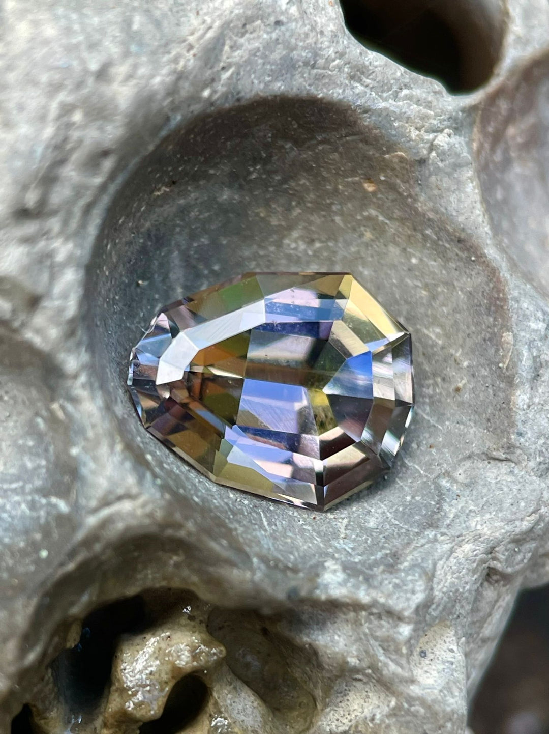Intriguing 2.10 carat Tanzanite gemstone nestled in a stone crevice, showcasing a custom geometric pear shape with a rich blend of purple, yellow, and green colors. Sourced from Merelani Hills, Tanzania, this gemstone demonstrates its unique hues and natural, untreated quality.