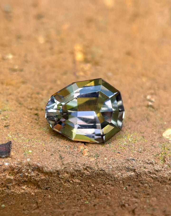 A 2.10 carat Tanzanite gemstone on a natural earth background, emphasizing its striking custom geometric pear shape and vivid colors of purple, yellow, and green. This premium Tanzanite from Merelani Hills, Tanzania, is shown in its raw and unenhanced state.