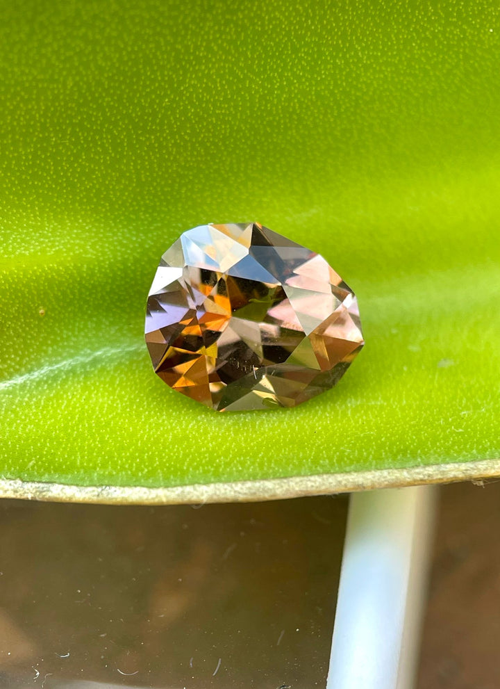 Exquisite Tanzanite gemstone resting on a green leaf, emphasizing its 2.43 carat weight, unique brown and champagne hues, and custom geometric pear shape. This natural and untreated gemstone from Tanzania is showcased in a vibrant, natural setting.