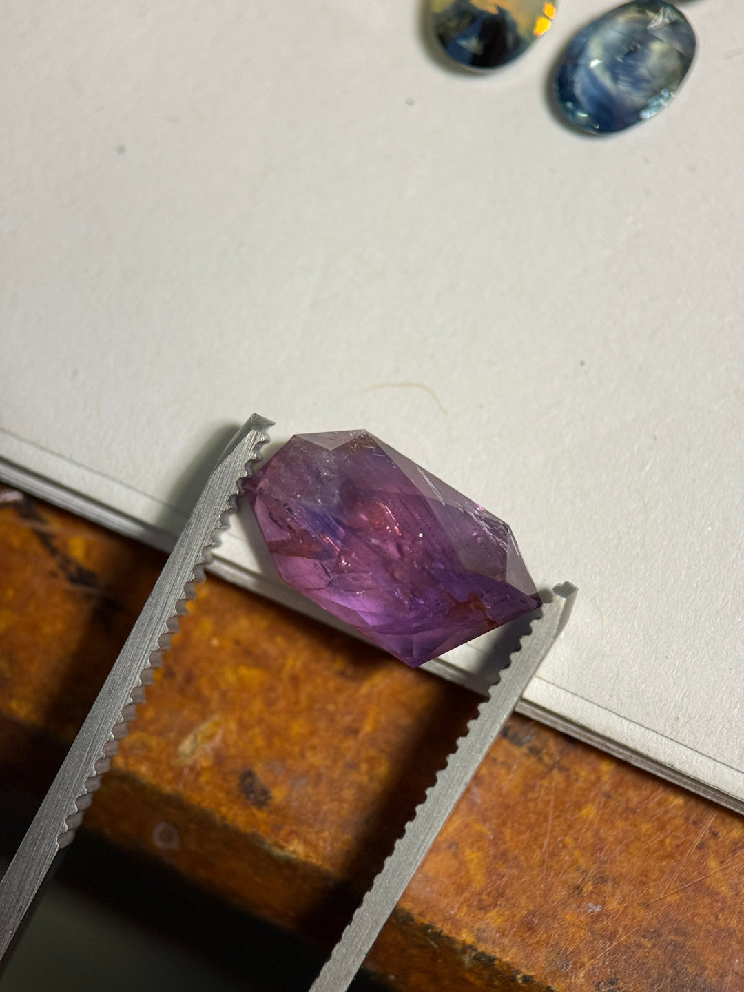 5.10ct Umba sapphire resting on white surface with pink-purple zoning and visible natural inclusions beneath the polished free-form crown.