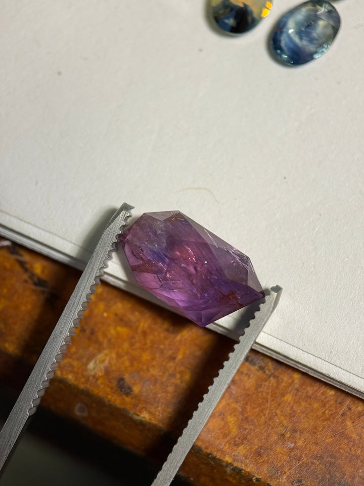 5.10ct Umba sapphire resting on white surface with pink-purple zoning and visible natural inclusions beneath the polished free-form crown.