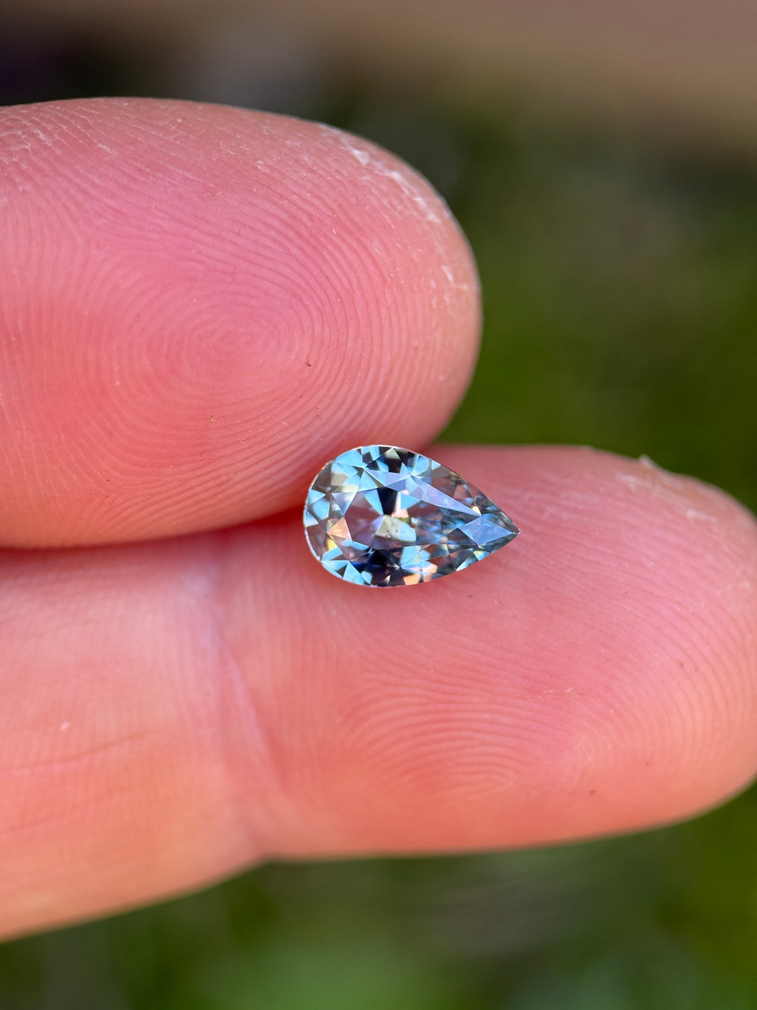 1.64ct periwinkle sapphire resting on fingertip, showing a soft blue-violet body color with bright flashes and crisp pear silhouette.