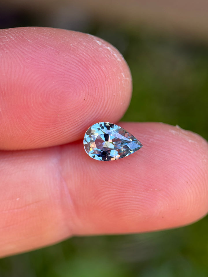 1.64ct periwinkle sapphire resting on fingertip, showing a soft blue-violet body color with bright flashes and crisp pear silhouette.