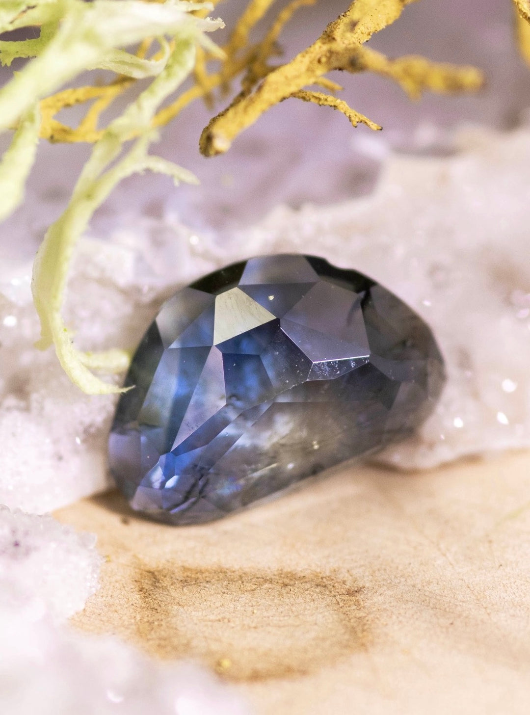 Custom trillion rose-cut sapphire nestled against pale textured stone, revealing dark blue edges fading into a warm yellow center under soft lighting.