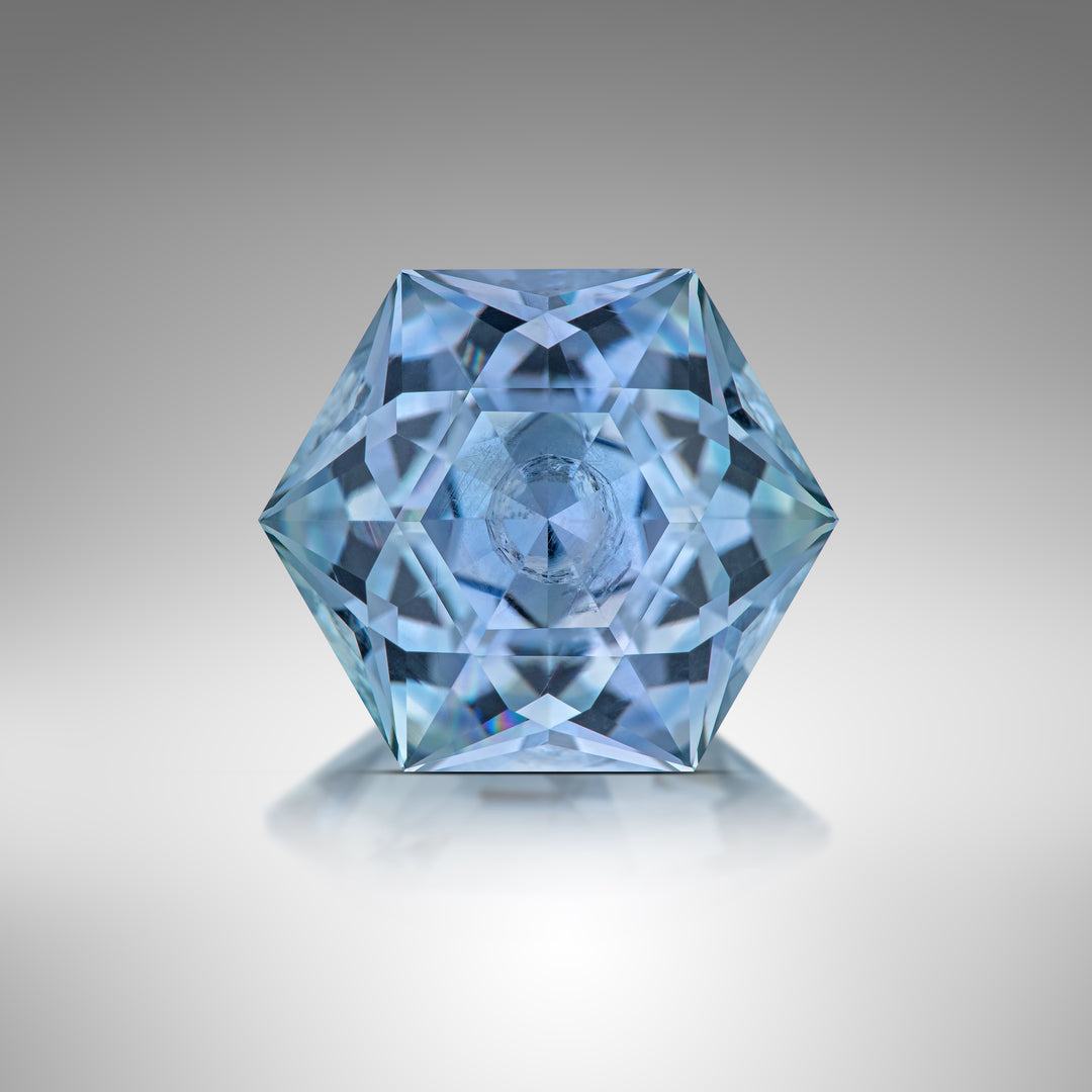 An exquisitely cut 5.79-carat hexagonal modified brilliant sapphire displayed on a smooth gradient background, showcasing its unique blend of green and blue hues. This rare gemstone is sourced from the El Dorado Bar Deposit in Montana, USA, and is completely untreated.