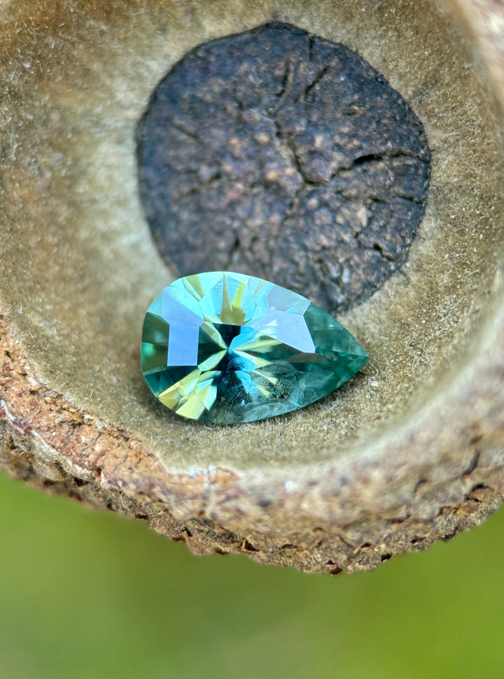 Lagoon teal green Montana sapphire resting inside a natural stone cavity, showcasing a 1.34 carat heated shield step cut sapphire with vivid green and teal color zoning.