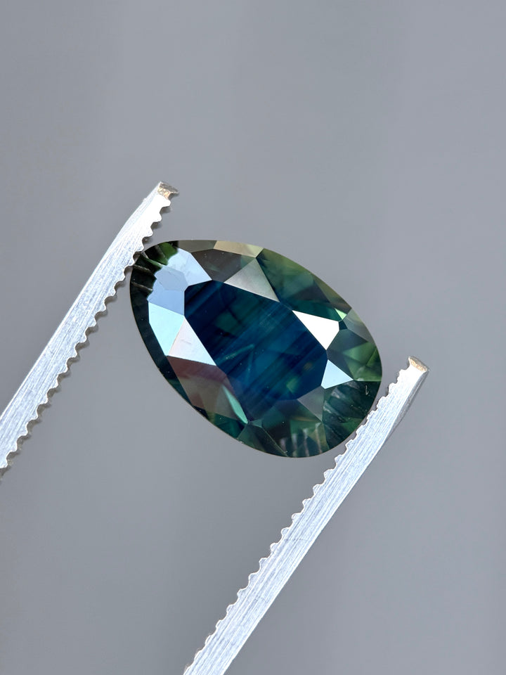 Close-up of teal sapphire displaying internal blue green zoning and brilliance in custom oval cut.