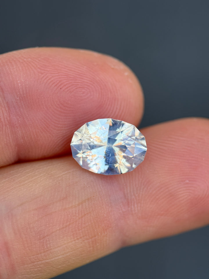 Large opalescent sapphire on fingertip showing size scale, soft earthy tones, and diffused internal glow.