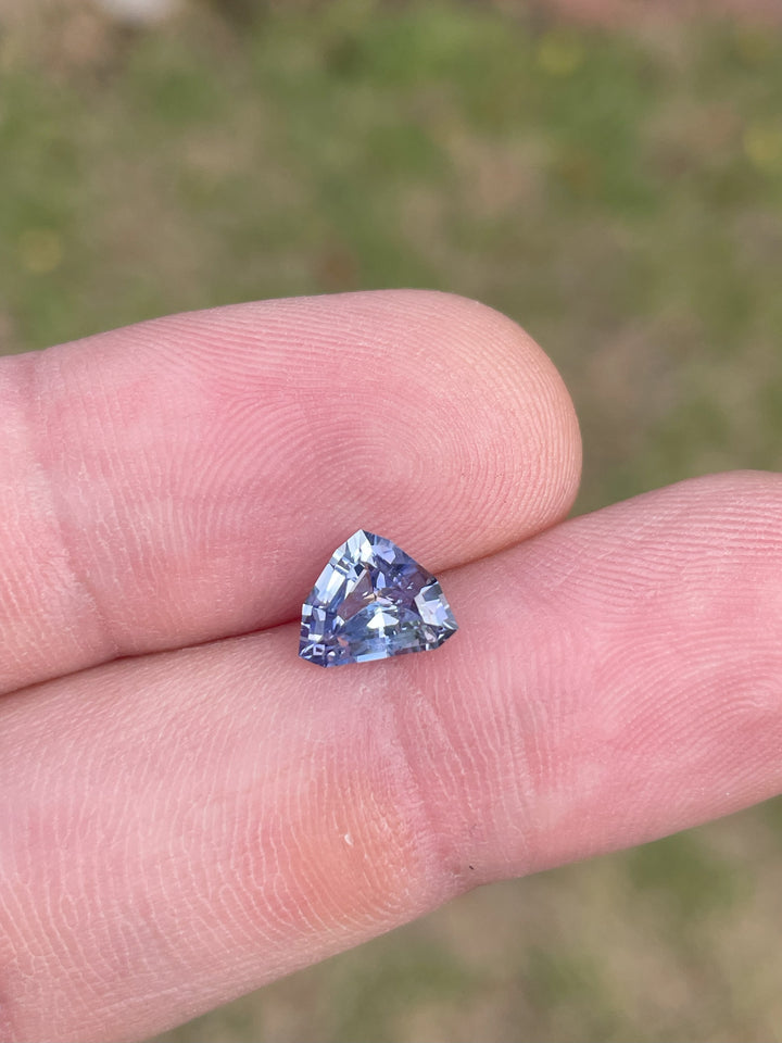 A 1.77-carat lavender and powder blue sapphire rests on a fingertip, showcasing its custom mix shield cut. The sapphire’s soft hues and precision cut make it stand out, with dimensions of 6.99mm by 8.73mm by 4.03mm. This untreated gem originates from Sri Lanka.
