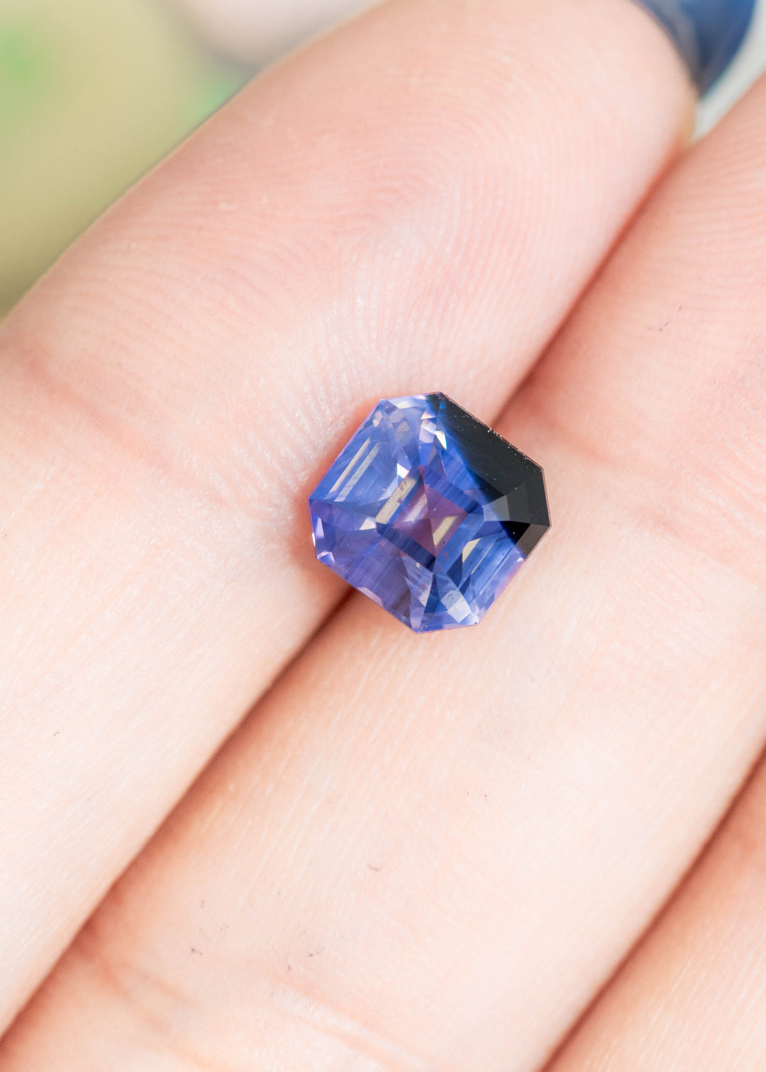 Loose opalescent lavender and periwinkle blue sapphire from Sri Lanka resting on fingertips showing the precision Asscher cut and natural color shift.