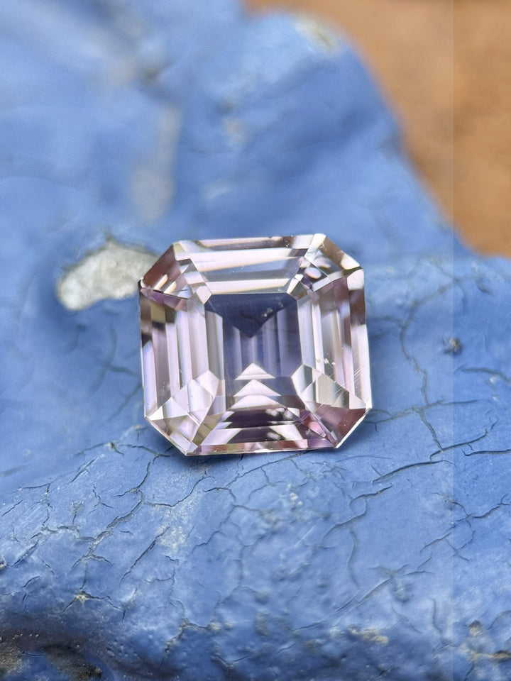 Close-up of 3.02 carat untreated Madagascar sapphire in pink-purple tones, custom emerald cut, photographed on textured blue surface to highlight contrast and brilliance.