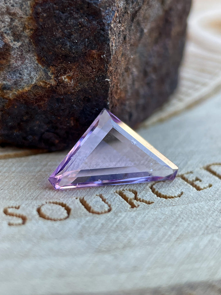 Lavender Spinel gemstone weighing 1.02 carats, featuring a trillion portrait cut, beautifully displayed on a rustic wooden surface.