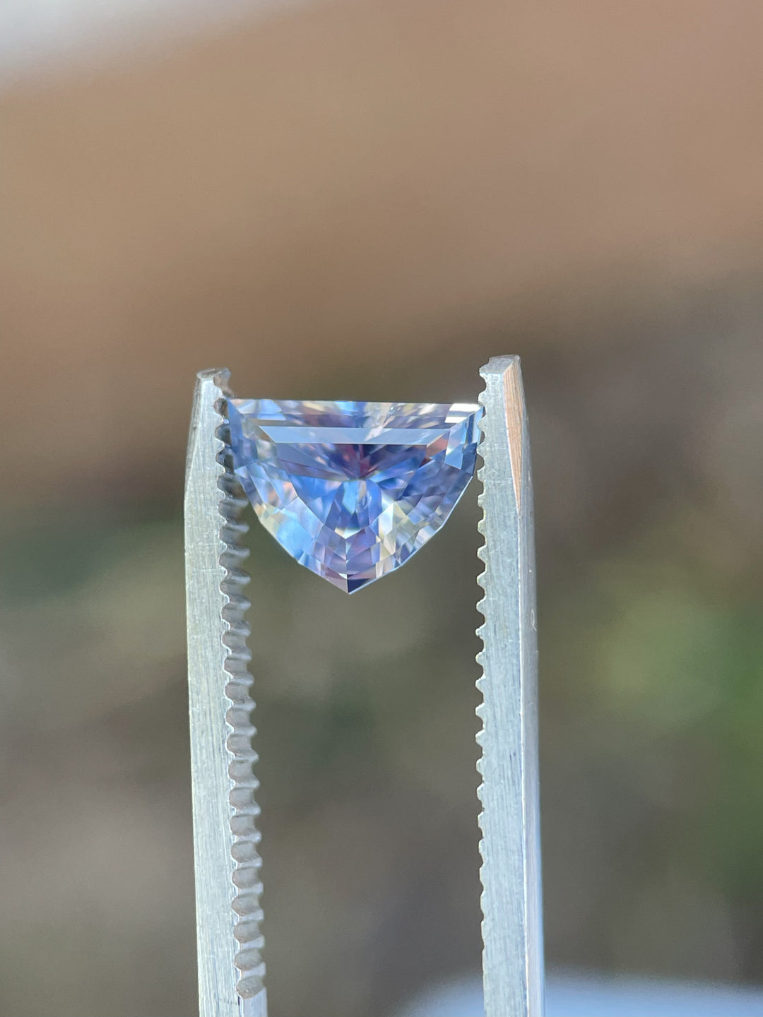 Lavender and pink sapphire secured in gem tweezers, displaying its unheated clarity and precision-cut facets.
