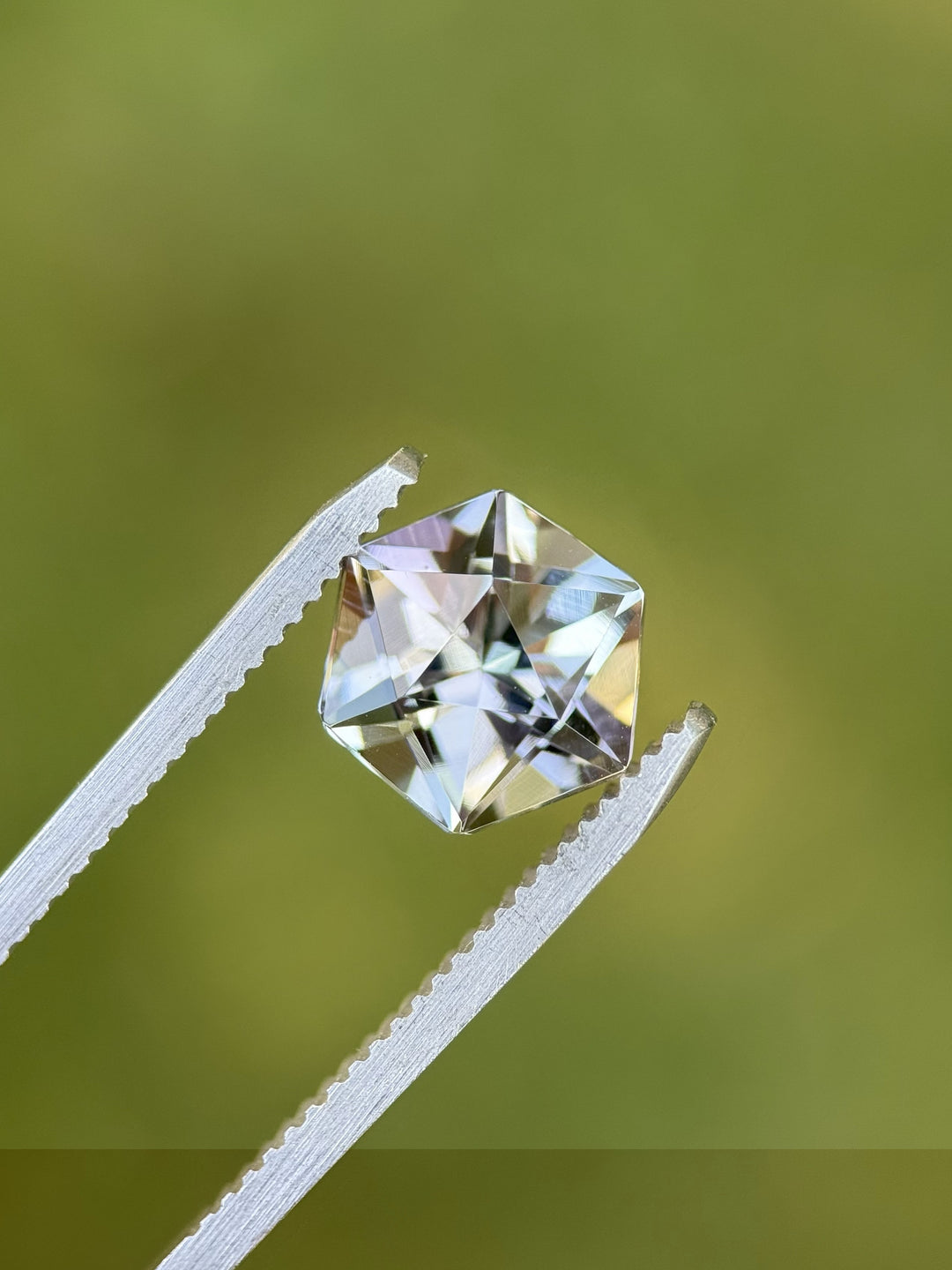 Hexagonal Tanzanite gemstone held in tweezers outdoors, displaying its multi-color play of lavender, blue, and teal.