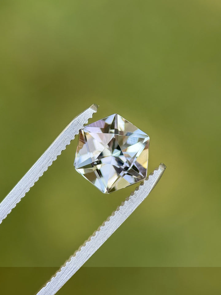 Hexagonal Tanzanite gemstone held in tweezers outdoors, displaying its multi-color play of lavender, blue, and teal.