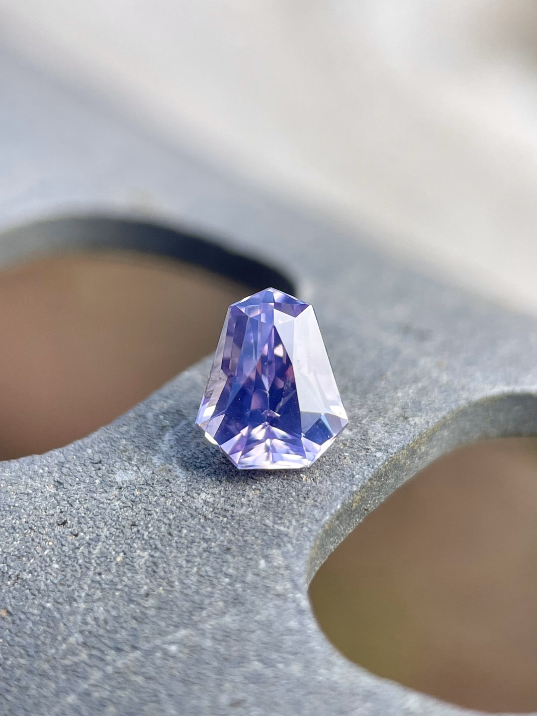 Vibrant 1.14 carat pink, lavender, and blue sapphire, custom shield cut, elegantly placed on a natural stone setting, reflecting its pristine clarity and Sri Lankan origin.
