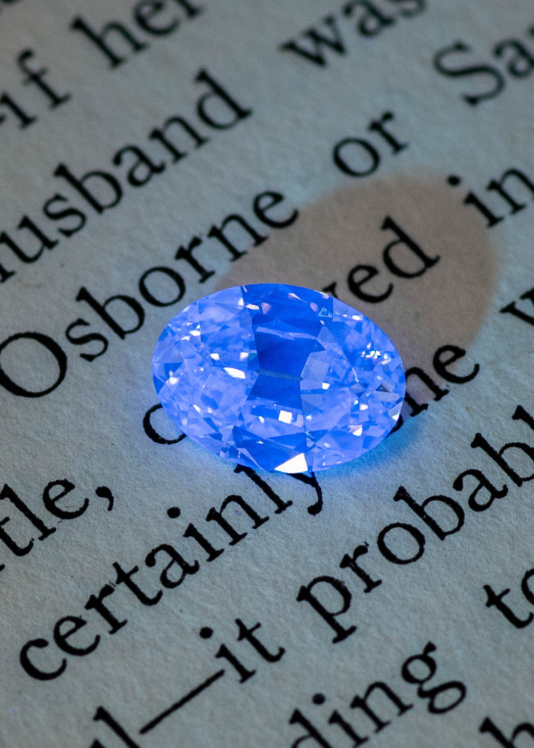 Oval diamond under UV light showing strong blue fluorescence against dark background, natural fluorescent diamond.