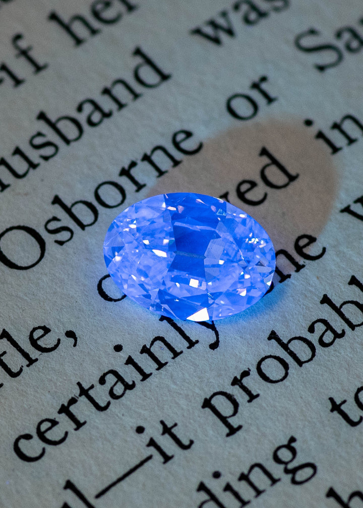 Oval diamond under UV light showing strong blue fluorescence against dark background, natural fluorescent diamond.