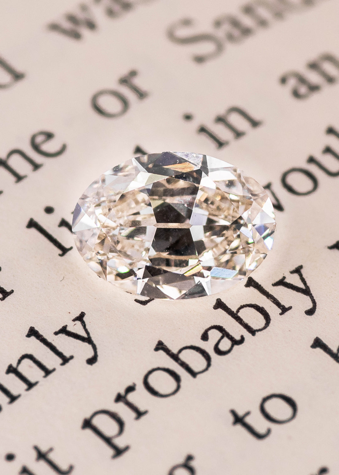 Oval modified brilliant diamond placed on book page highlighting natural color and facet reflections, loose Canadian diamond.