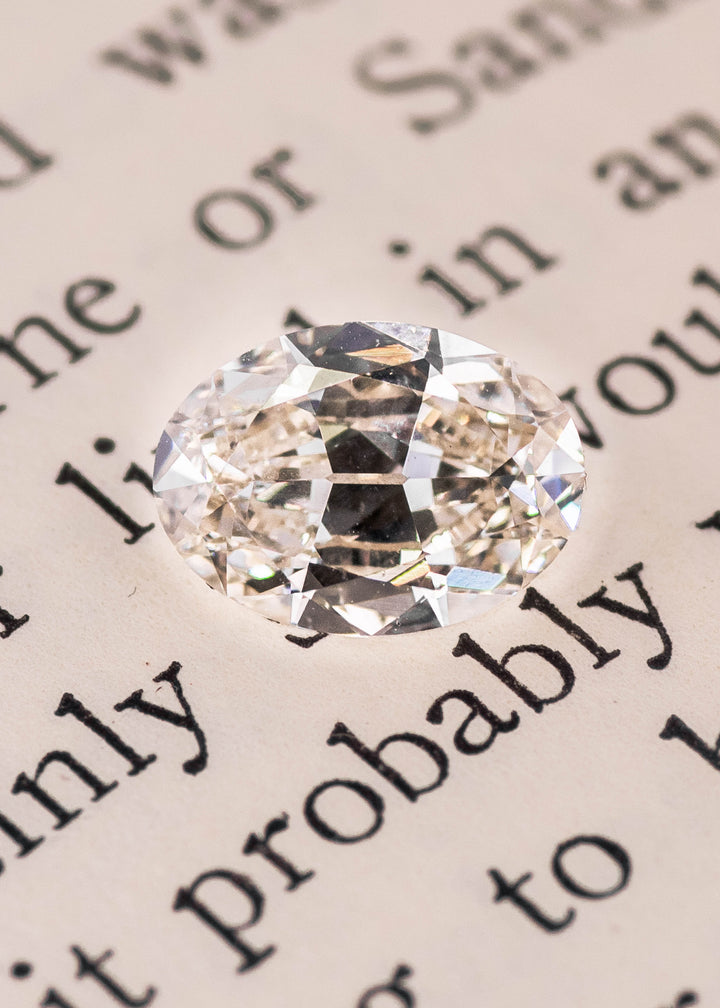 Oval modified brilliant diamond placed on book page highlighting natural color and facet reflections, loose Canadian diamond.