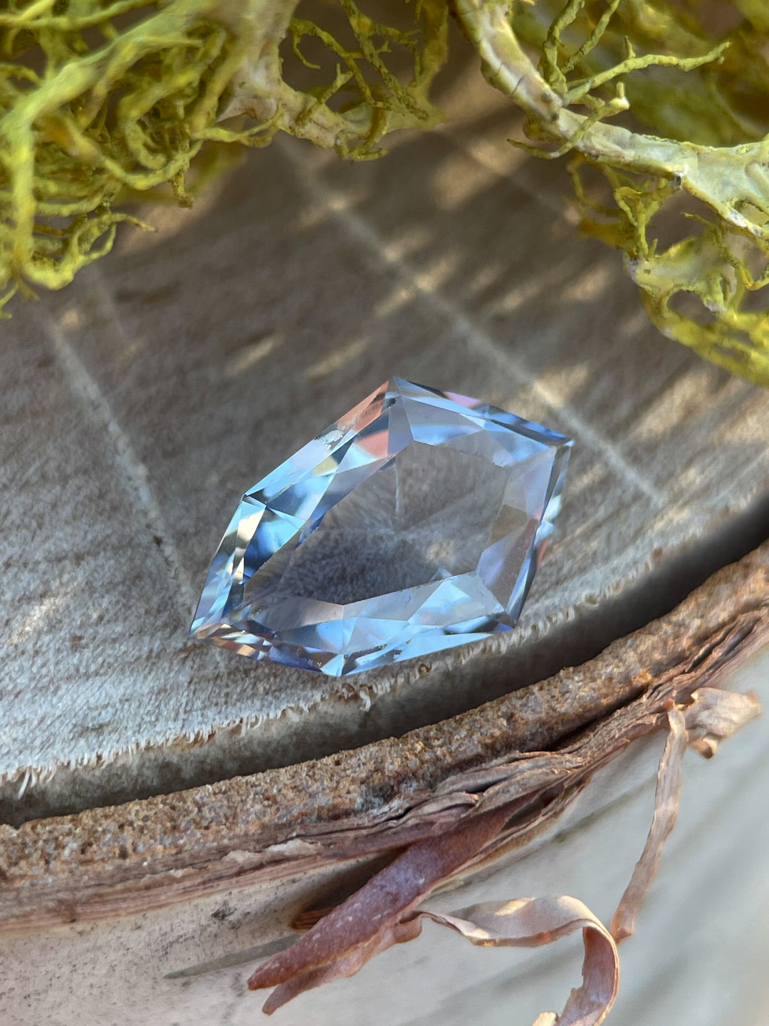 A stunning 1.66-carat custom mix shield-cut sapphire in light Ceylon denim blue resting on a rustic surface, originating from Sri Lanka with no heat treatment.
