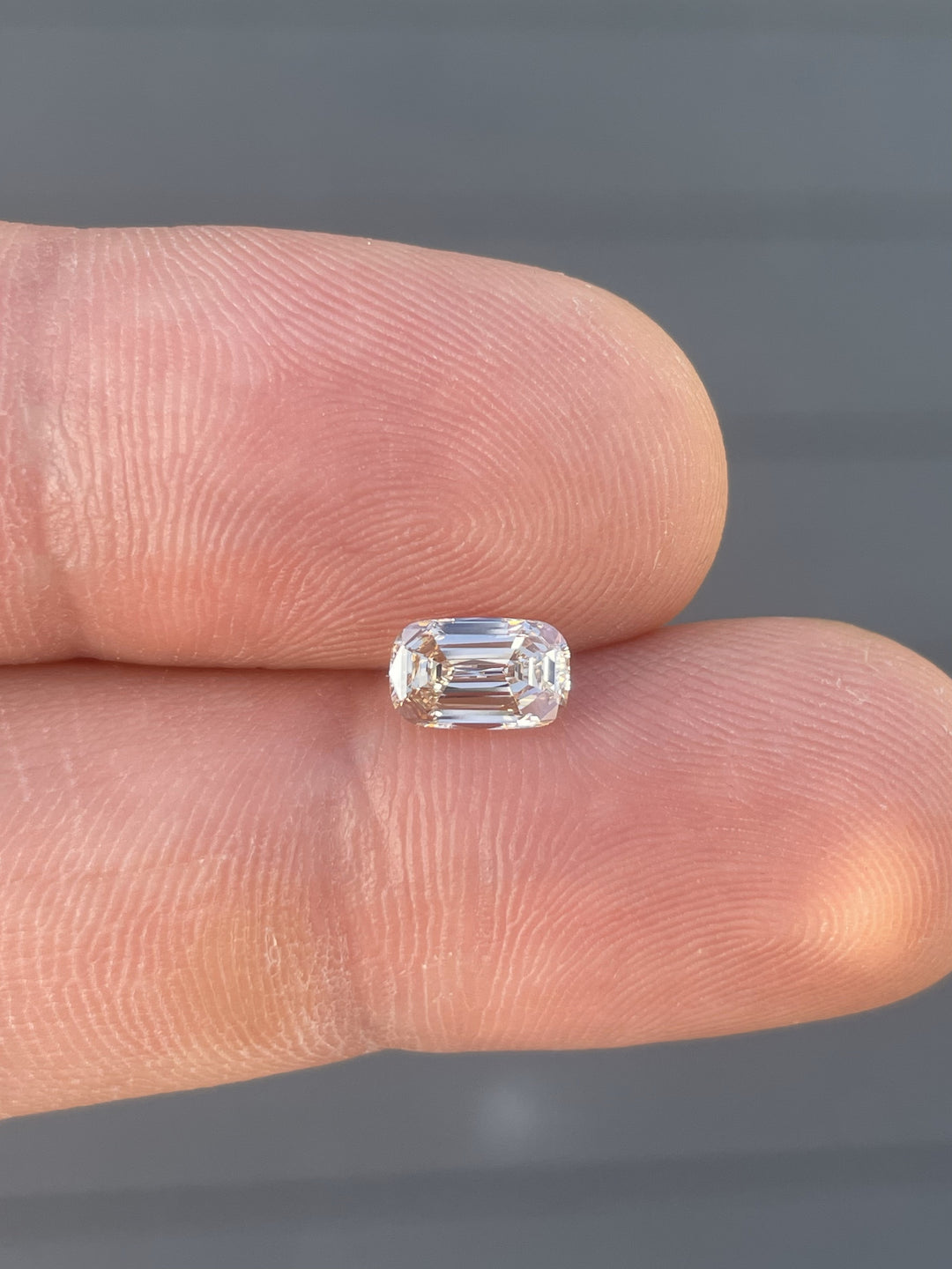 A light fancy yellowish brown 1.02-carat cushion cut diamond held in fingers, showcasing its intricate facets and warm tones against a natural outdoor backdrop.